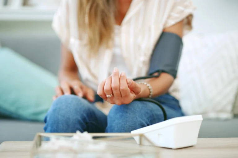 Mulher sentada no sofá medindo a pressão, ilustrando a dúvida entre aparelho de pressão digital ou analógico