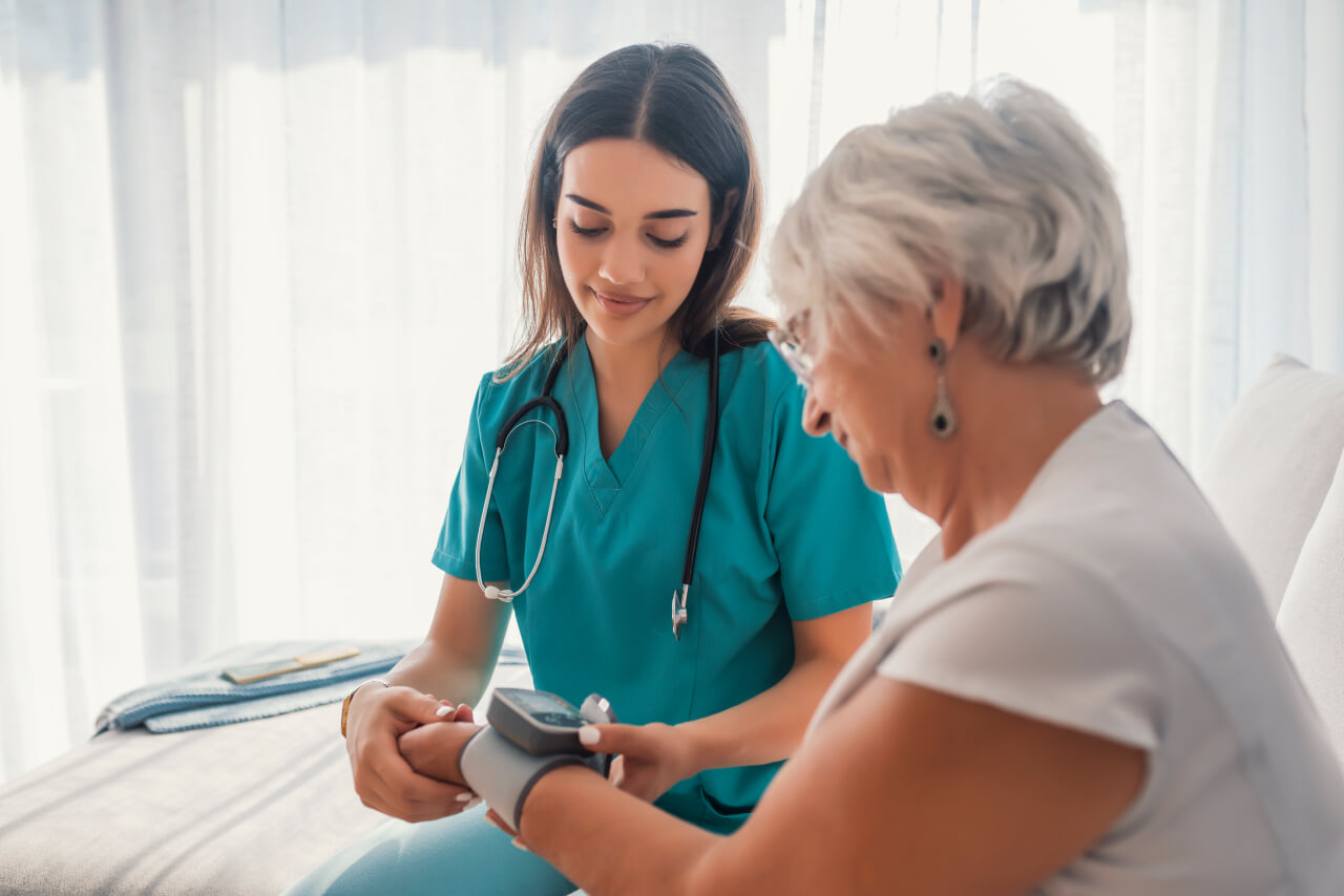 Imagem de uma médica atendendo paciente com produtos para Home Care, como estetoscópio e aparelho de pressão.