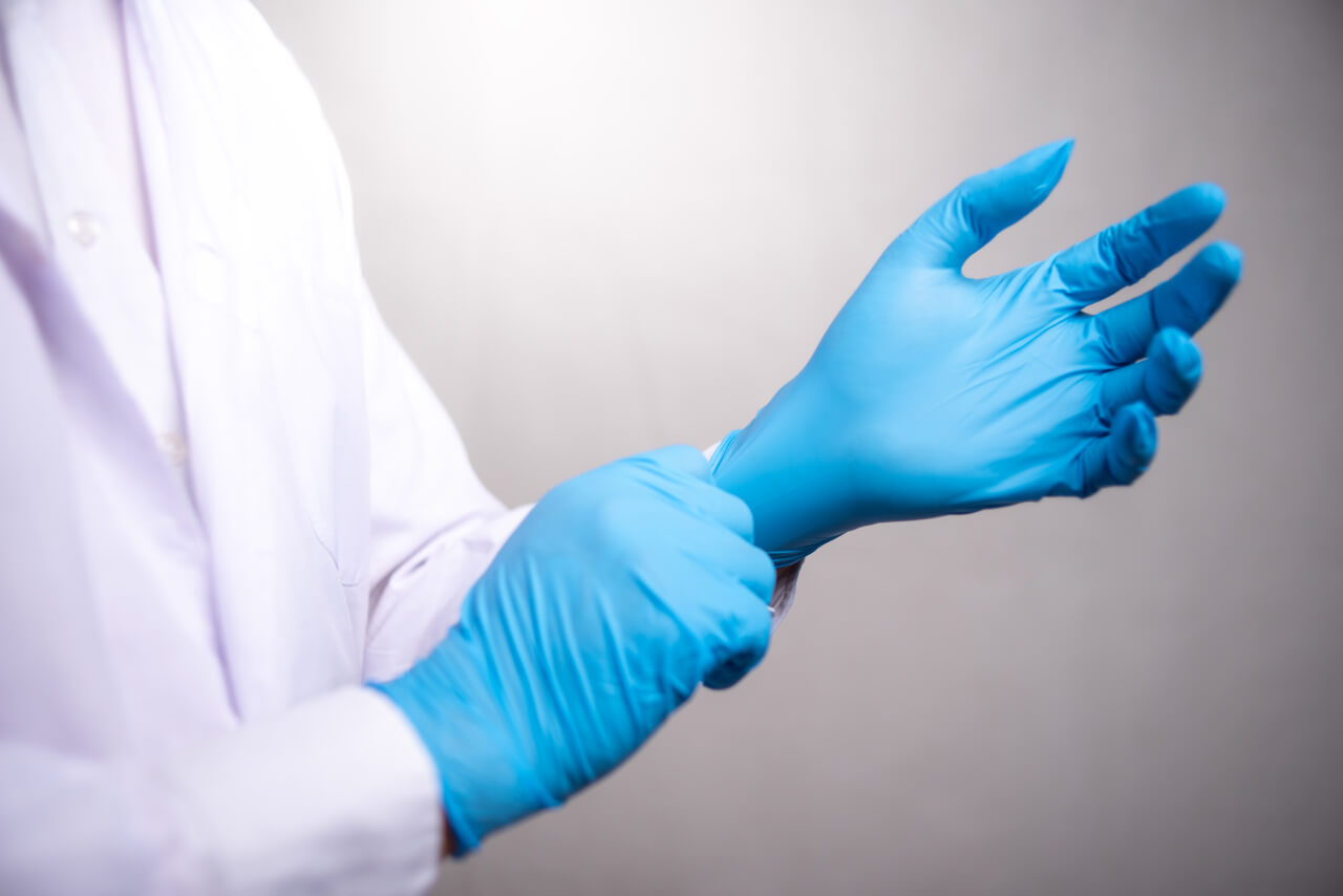 Imagem de um médico calçando um dos diferentes tipos de luvas hospitalares antes de um procedimento clínico.