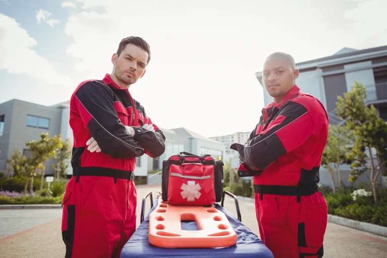 Imagem de dois socorristas em frente a uma maca e kit de emergência, simbolizando o atendimento pré-hospitalar.