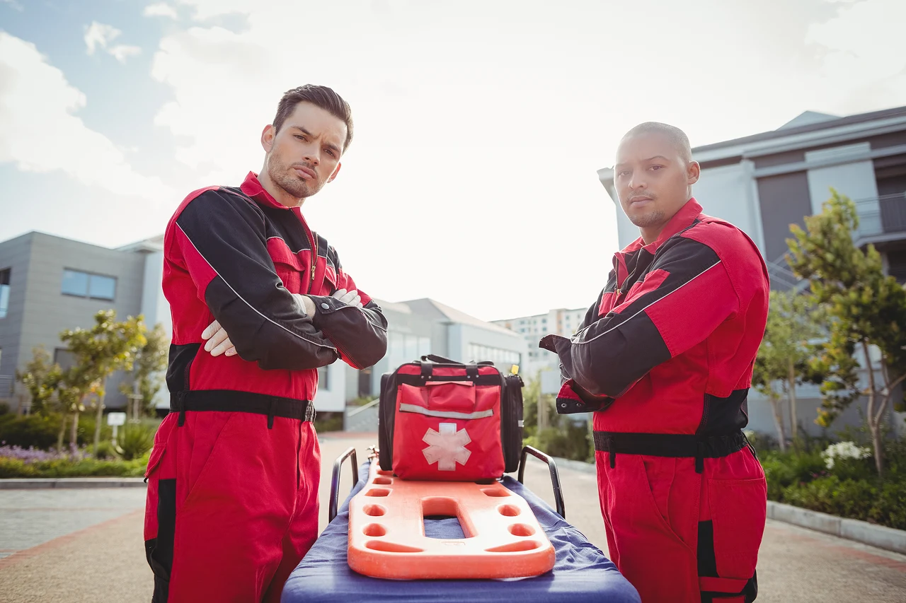 Imagem de dois socorristas em frente a uma maca e kit de emergência, simbolizando o atendimento pré-hospitalar.
