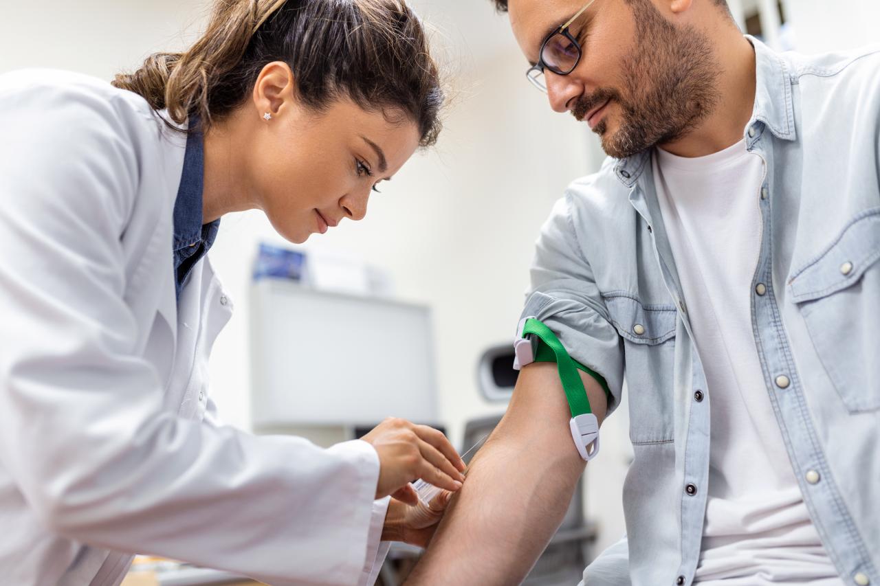 Profissional realiza coleta de sangue em paciente com garrote no braço em ambiente clínico